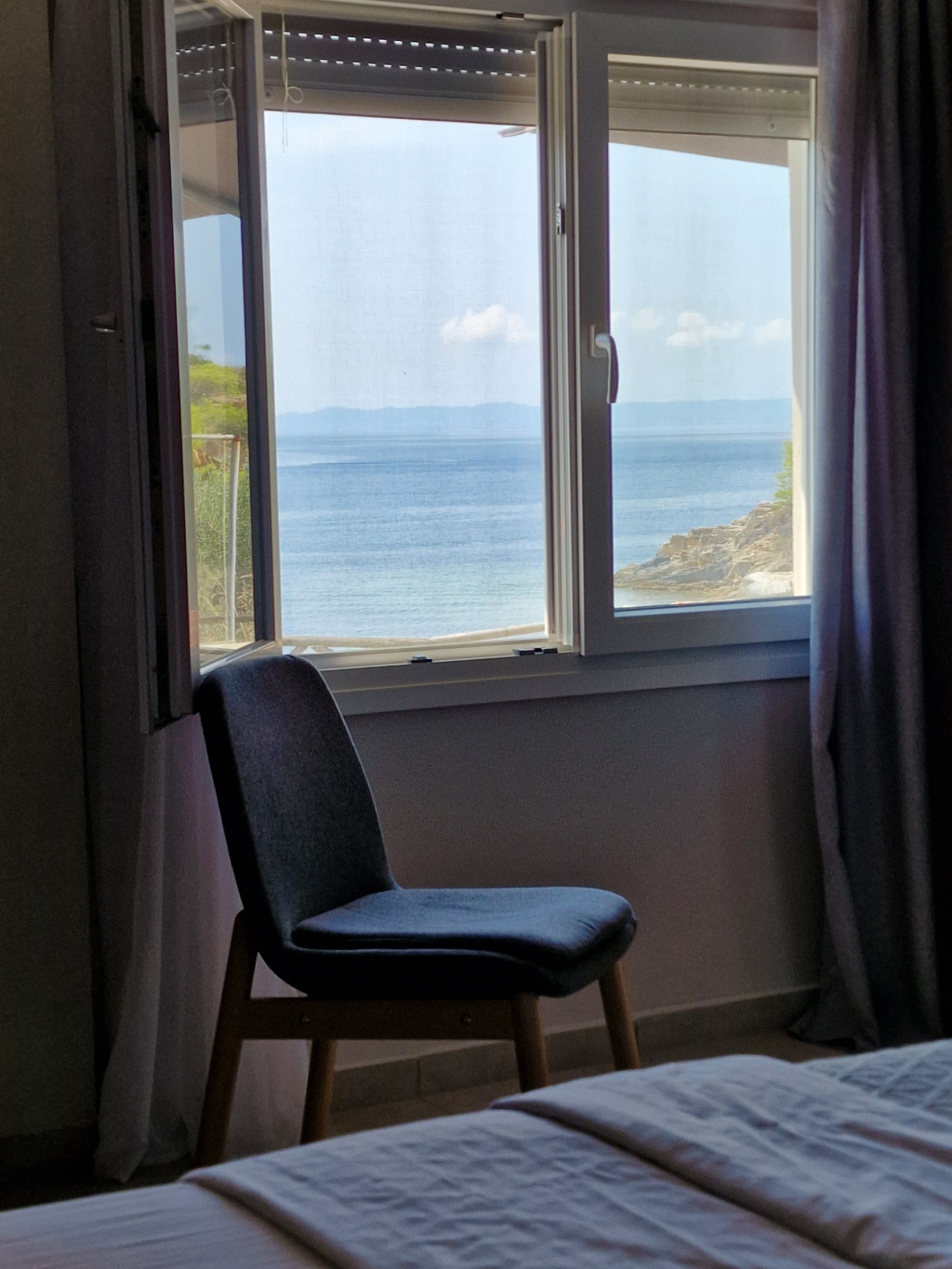 Grey armchair beside the bedroom window with the Aegean beyond