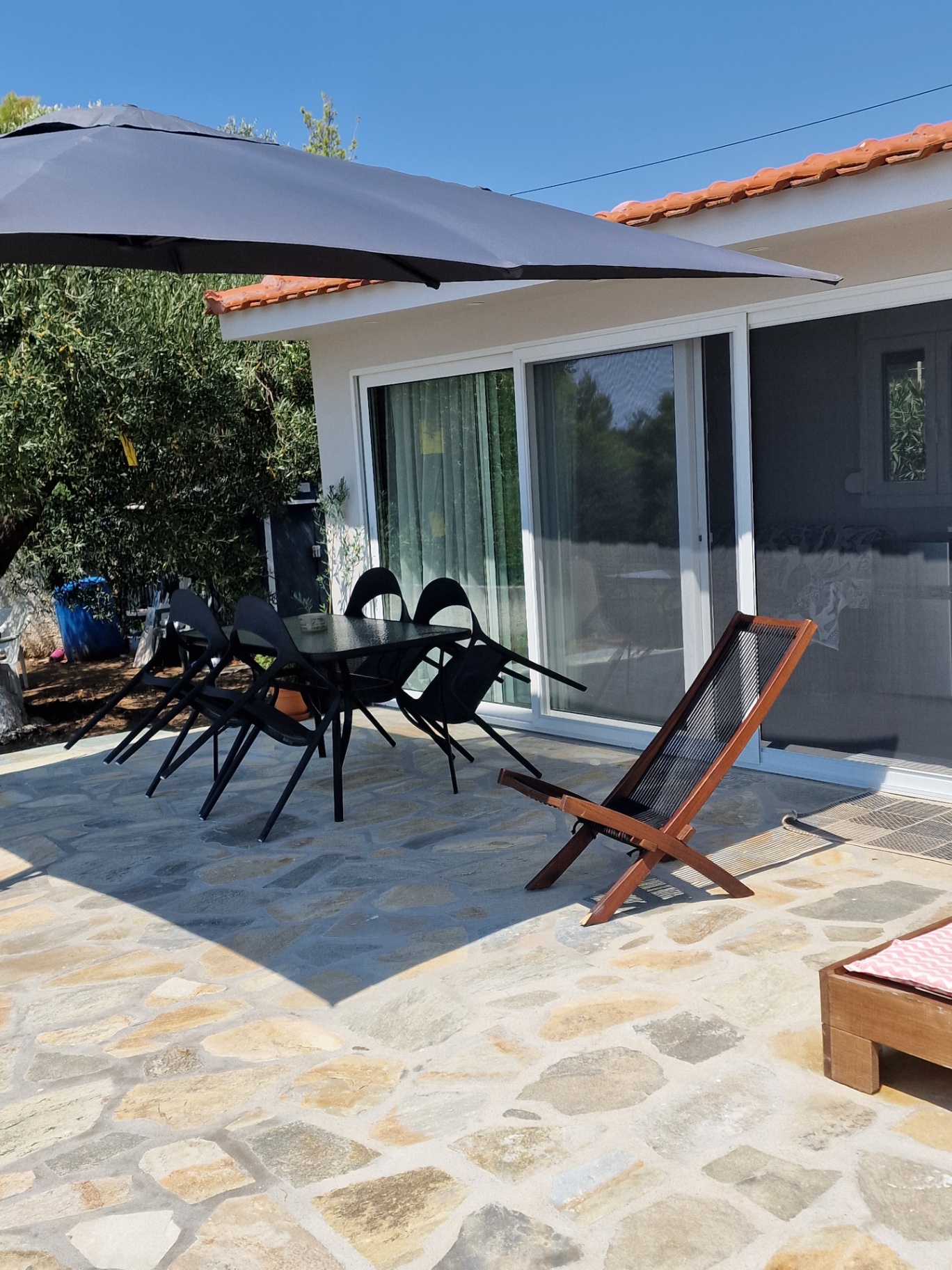 Black table and chairs under the parasol beside a wooden lounger on the stone terrace