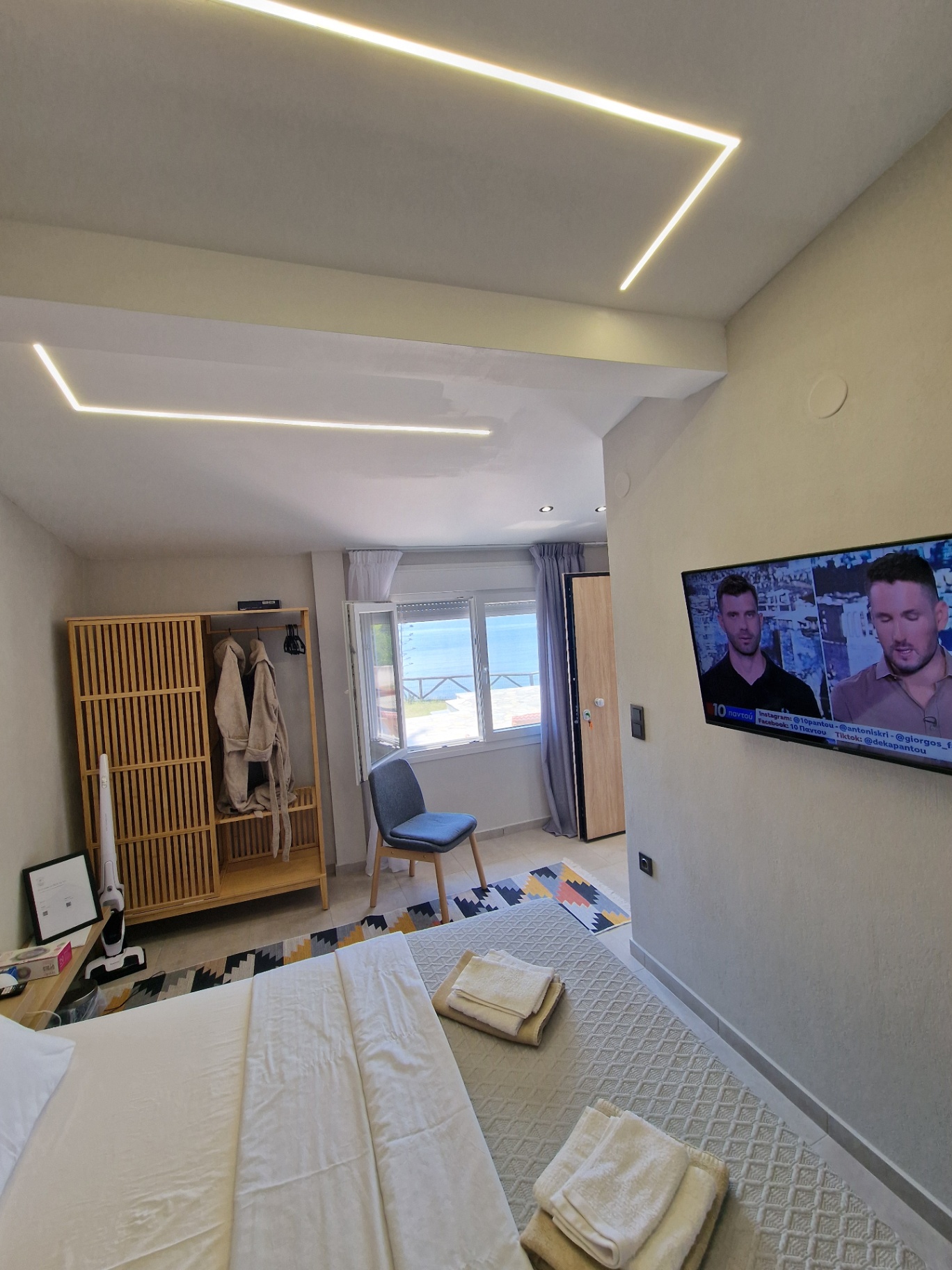 The bedroom seen wide, with wardrobe, television and the sea through the window