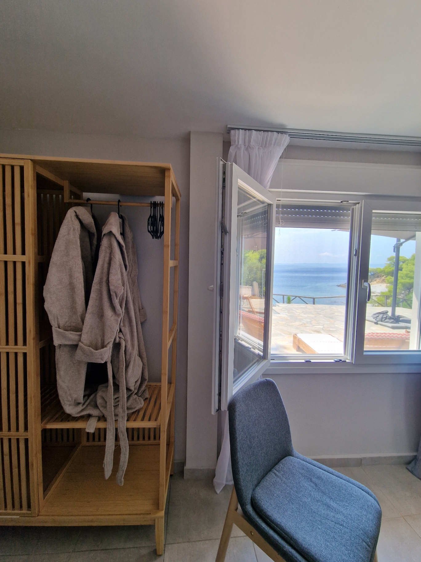 Bamboo wardrobe with robes beside the open window and the sea