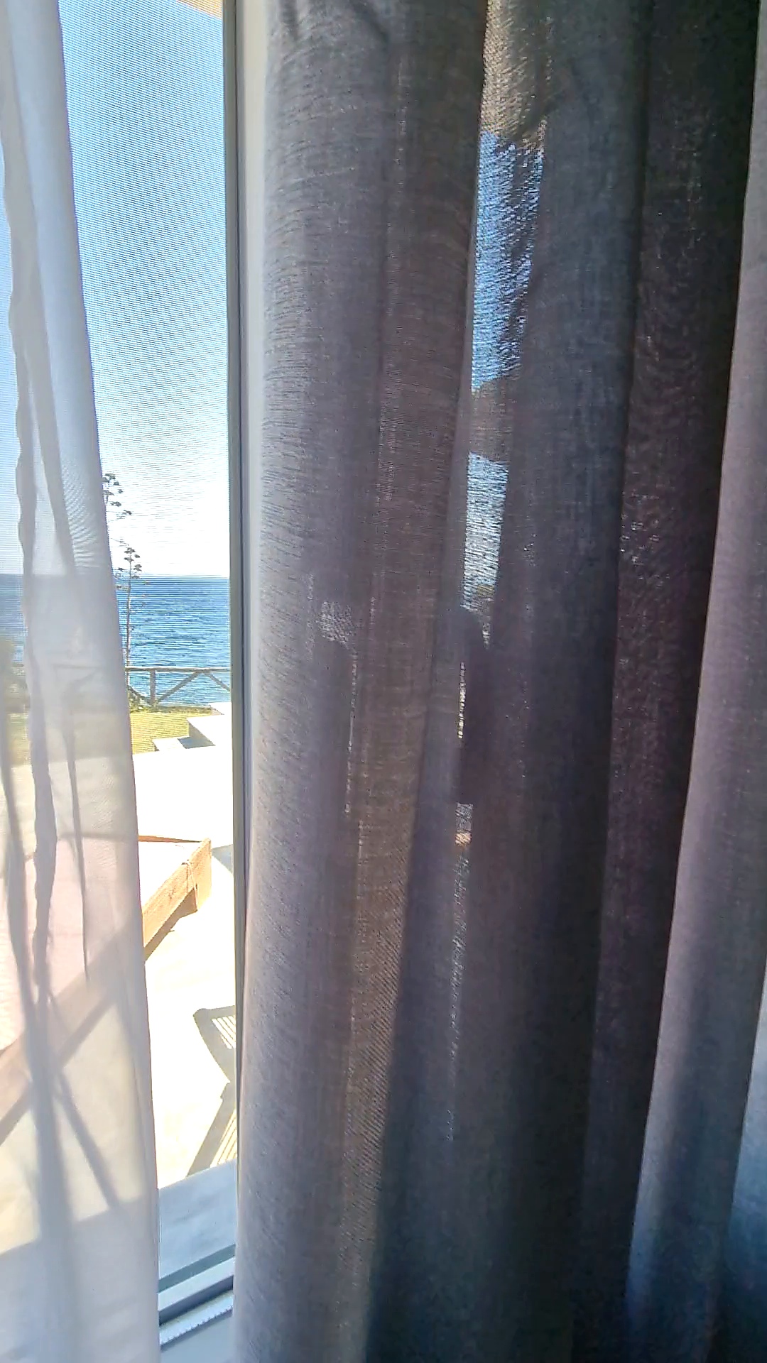 Daylight and the terrace behind soft grey curtains